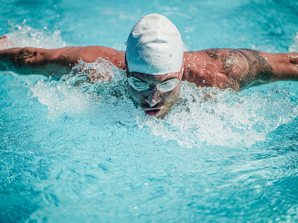 atleta con cuffia bianca e occhialini che fa una bracciata a delfino in piscina
